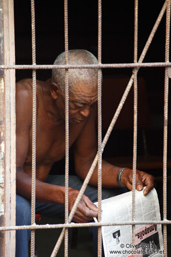 Man reading the newspaper behind bars in Havana Vieja