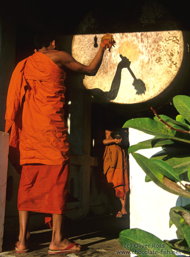 Buddhist monk novice performing the drumming ritual just before sunset